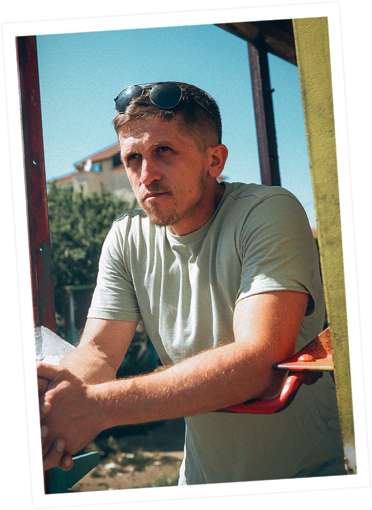 Florent Osmani blickt ernst in die Ferne. Er trägt eine Sonnenbrille auf dem Kopf. Er befindet sich draußen vor einem Haus.