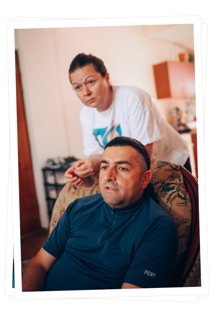 Dragan sitzt auf einem Stuhl, während seine Frau Dijana hinter ihm steht. Beide blicken konzentriert. 