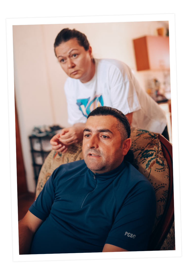 Dragan sitzt auf einem Stuhl, während seine Frau Dijana hinter ihm steht. Beide blicken konzentriert. 