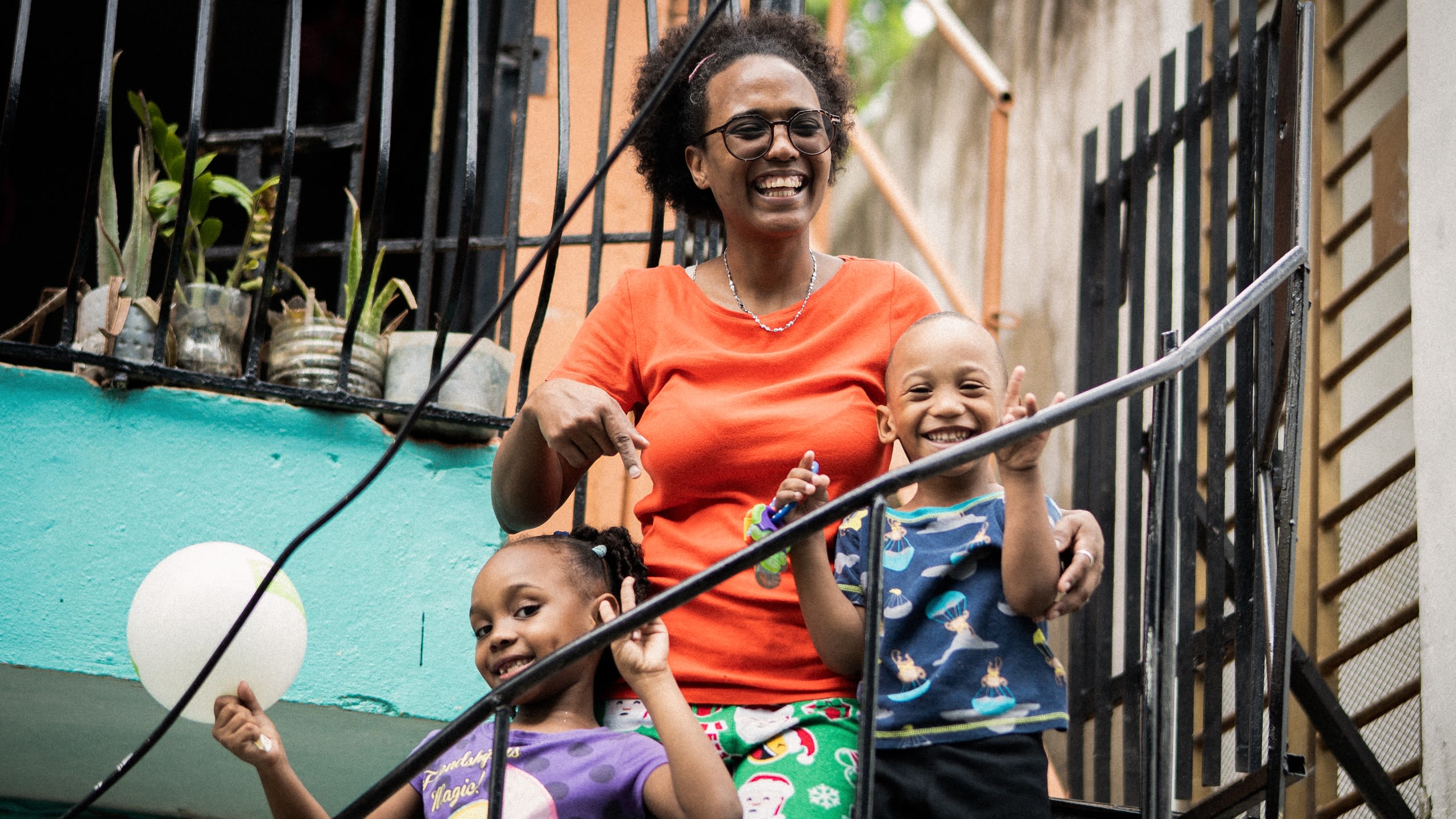 Foto von Evelin Martinez mit ihren beiden Kindern auf einer Treppe, sie lachen und winken fröhlich in die Kamera.