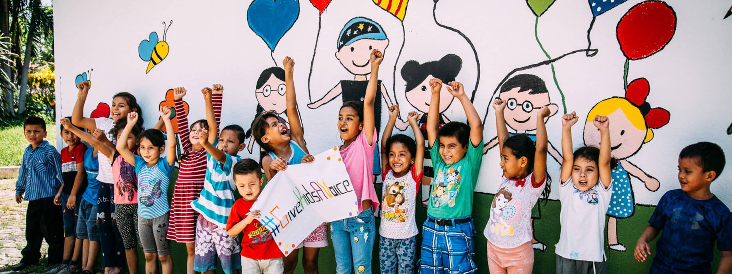 Viele Kinder strecken vor einer bemalten Wand die Hände hoch und setzen sich für Kinderrechte ein.