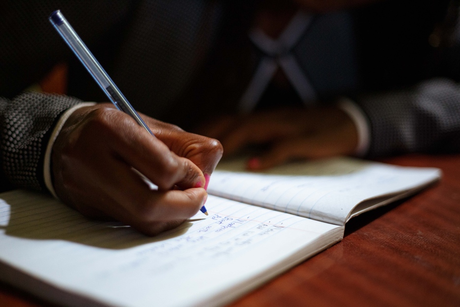 Die Hand eines Schwarzen Mädchens, die in ein Heft schreibt.