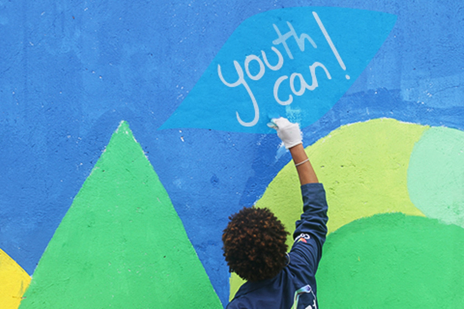 Junge, der auf eine bunte Mauerwand die Worte ,youth can!‘ schreibt