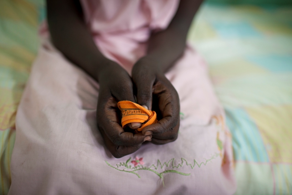 Nahaufnahme der Hände eines Kindes im Sudan, das ein orangefarbenes Stoffband hält; das Bild steht für die Verletzlichkeit von Kindern in der aktuellen humanitären Krise.