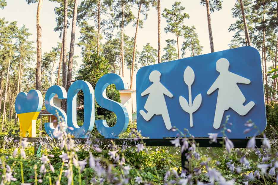 Großaufnahme: Das Logo der SOS-Kinderdörfer in der Ukraine vor Bäumen. Foto: Olek-sandra Zborovska