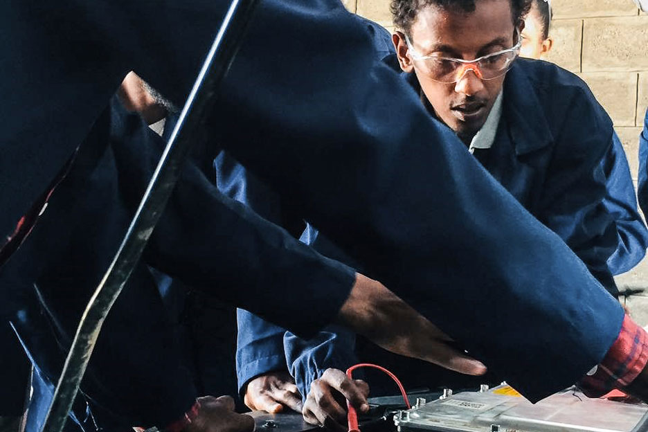 Auszubildende des Pilotprojekts der SOS-Kinderdörfer in Äthiopien beugen sich über die geöffnete Motorhaube eine E-Autos.