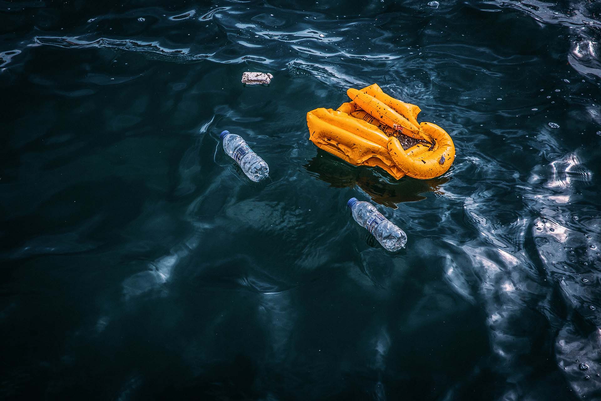 Eine gelbe Schwimmweste treibt im Meer, daneben leere Wasserflaschen.