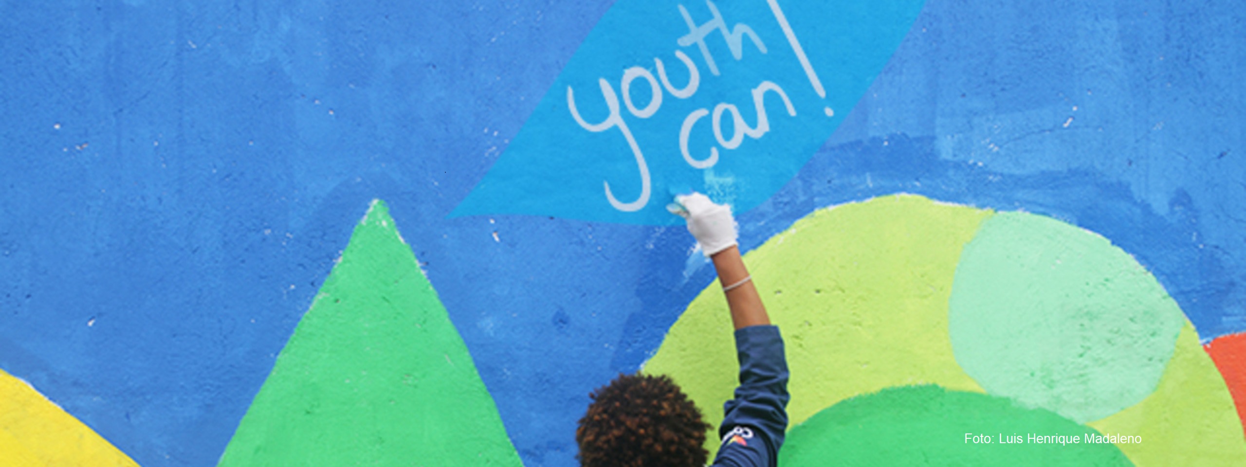 Ein Junge malt an eine bunte Wand den Slogan Youth Can