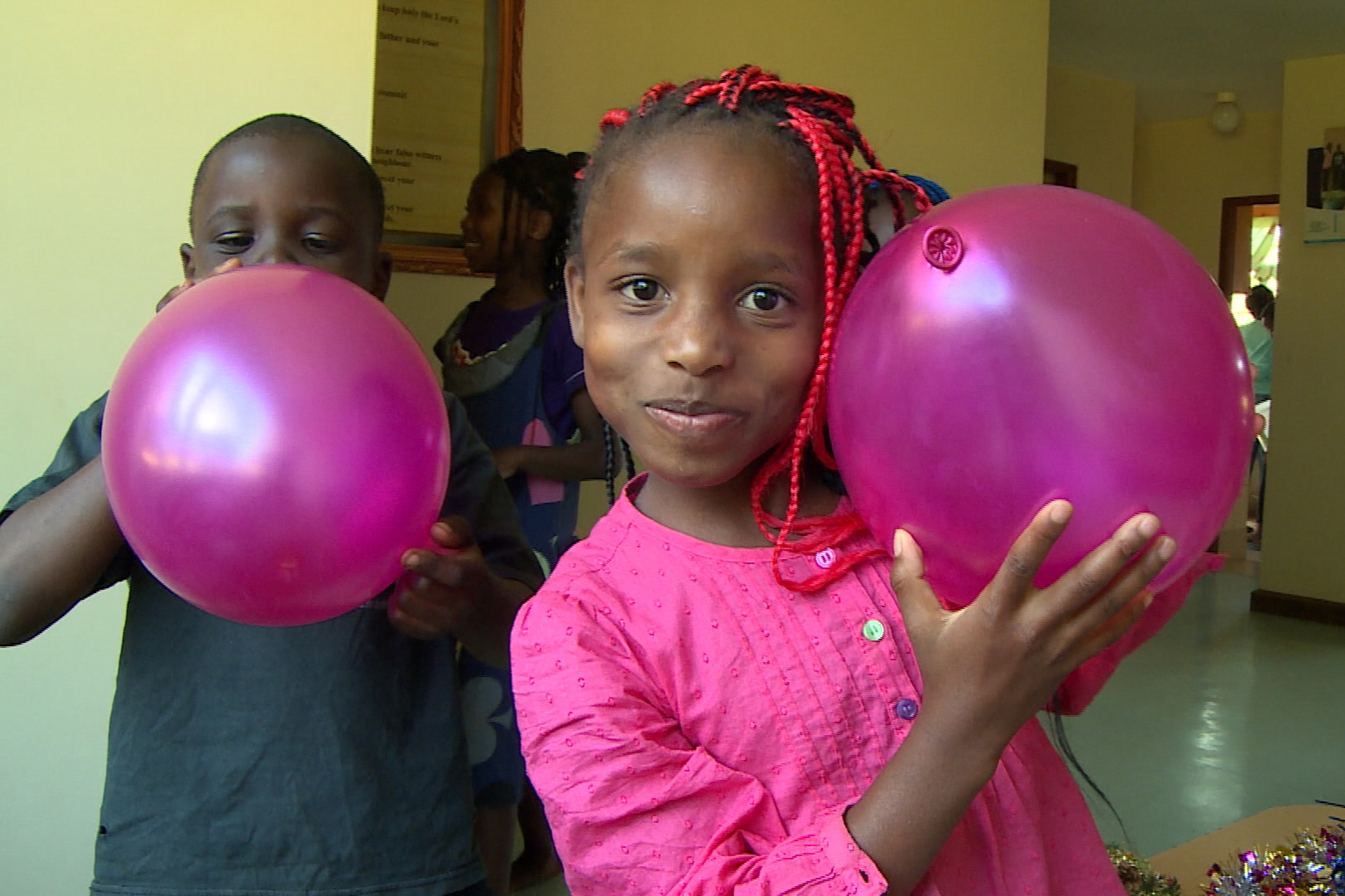 Zwei Kinder haben pinke Luftballons in ihren Händen, das Mädchen vorne hat zudem pinke geflochtene Haare.