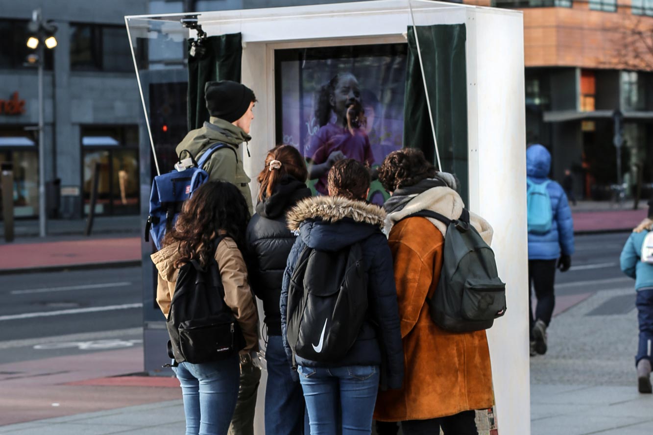 Passant:innen vor einem Video-Screen