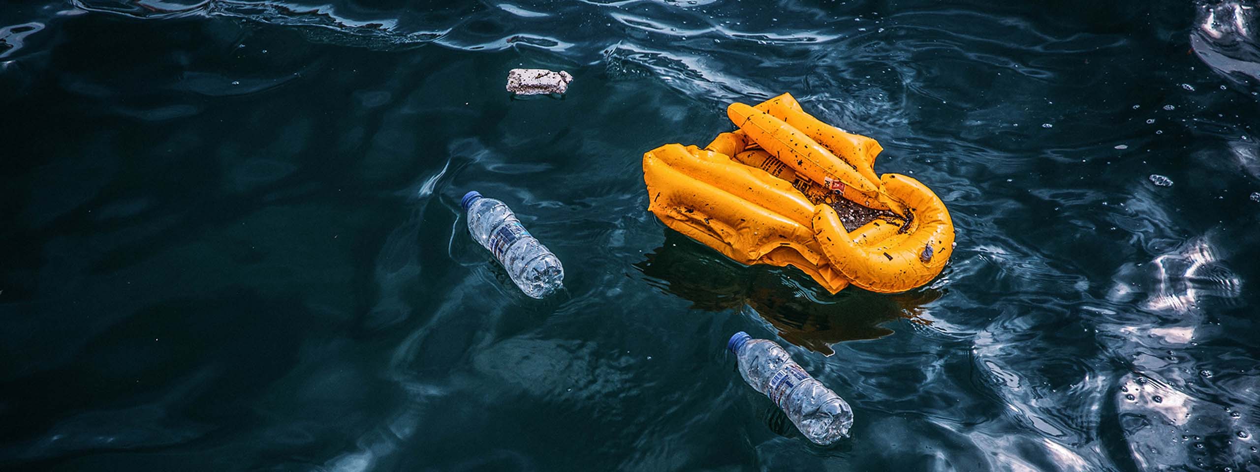 Auf dem Meer treibt eine gelbe Schwimmweste, daneben leere Wasserflaschen.
