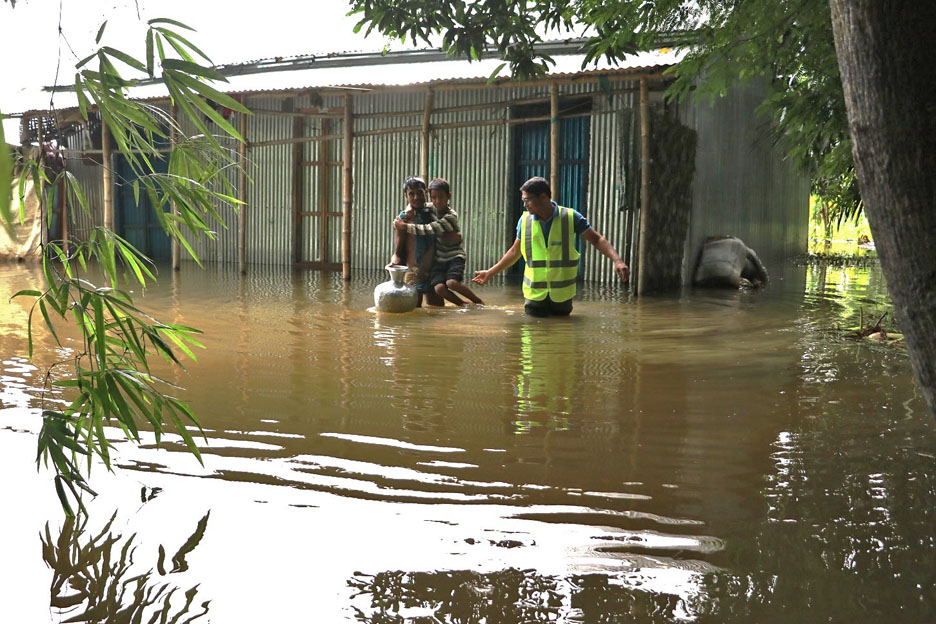 Rekordflut in Bangladesch im Juni 2022: Ein Helfer der SOS-Kinderdörfer und ein Mann mit Kind auf dem Arm waten durchs Wasser. Foto: SOS-Kinderdörfer