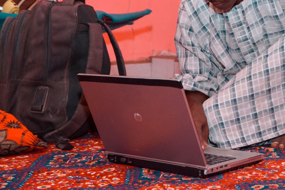 Ein sudanesisches Mädchen sitzt im Schneidersitz auf einem Teppich vor einem aufgeklappten Laptop.