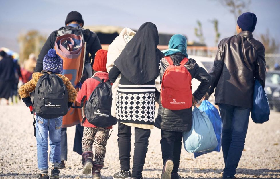 Eine Gruppe von Kindern und Erwachsenen läuft, bepackt mit Rucksäcken und Tüten, eine Straße entlang.