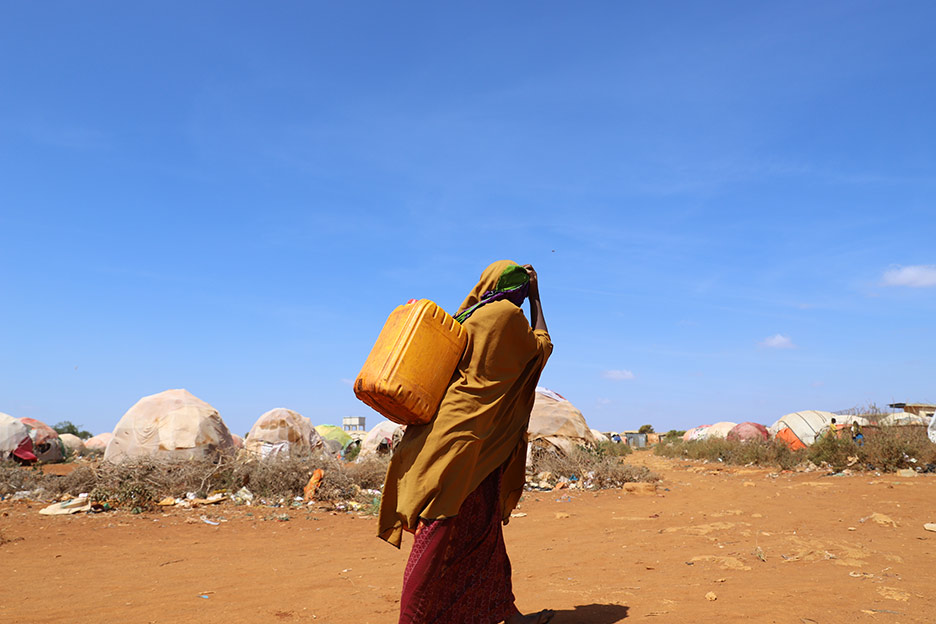 Eine Frau läuft mit einem Wasserkanister auf dem Rücken am Stadtrand von Baidoa City, Somalia