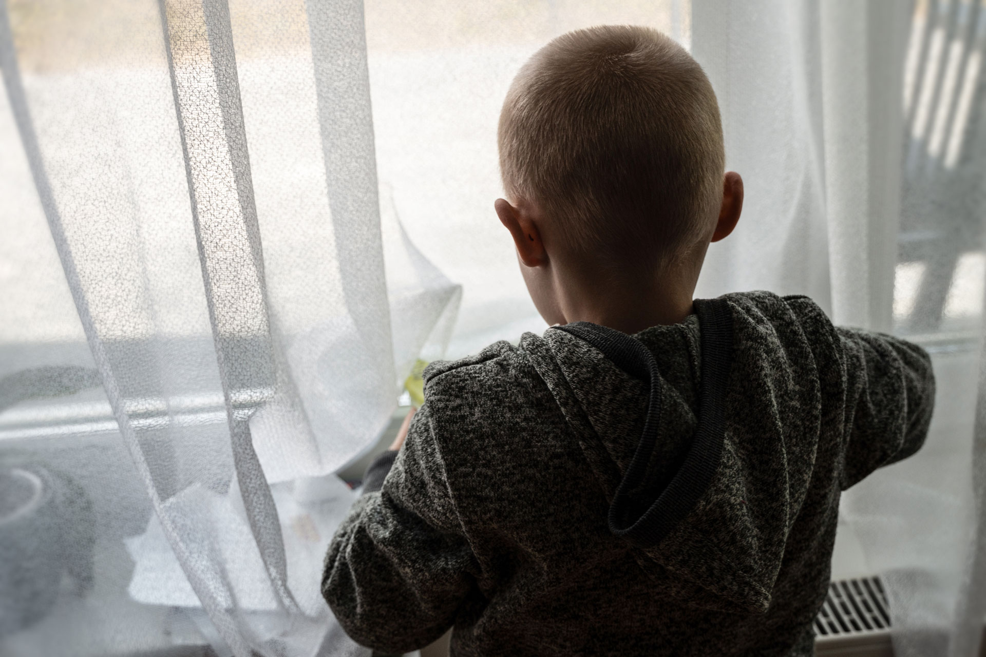 Ukrainisches Kind schaut hinter Gardinen aus dem Fenster.