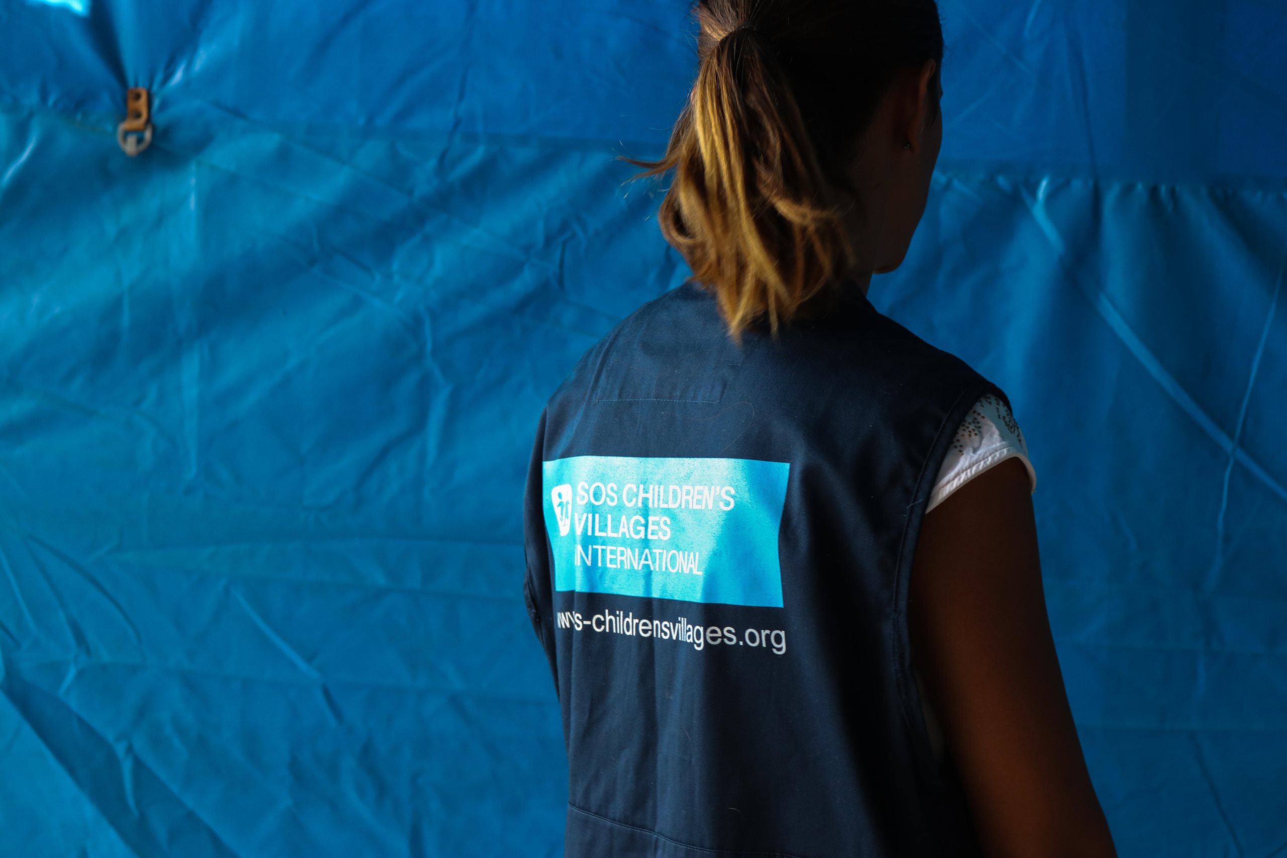 Ein Helfender der SOS-Kinderdörfer steht mit dem Rücken vor einer blauen Wand.