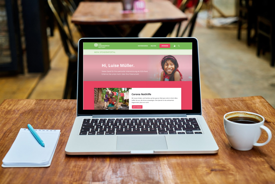 Tisch mit Block und Stift, einem Laptop, der das SOS-Kinderdörfer Portal zeigt und Kaffee 