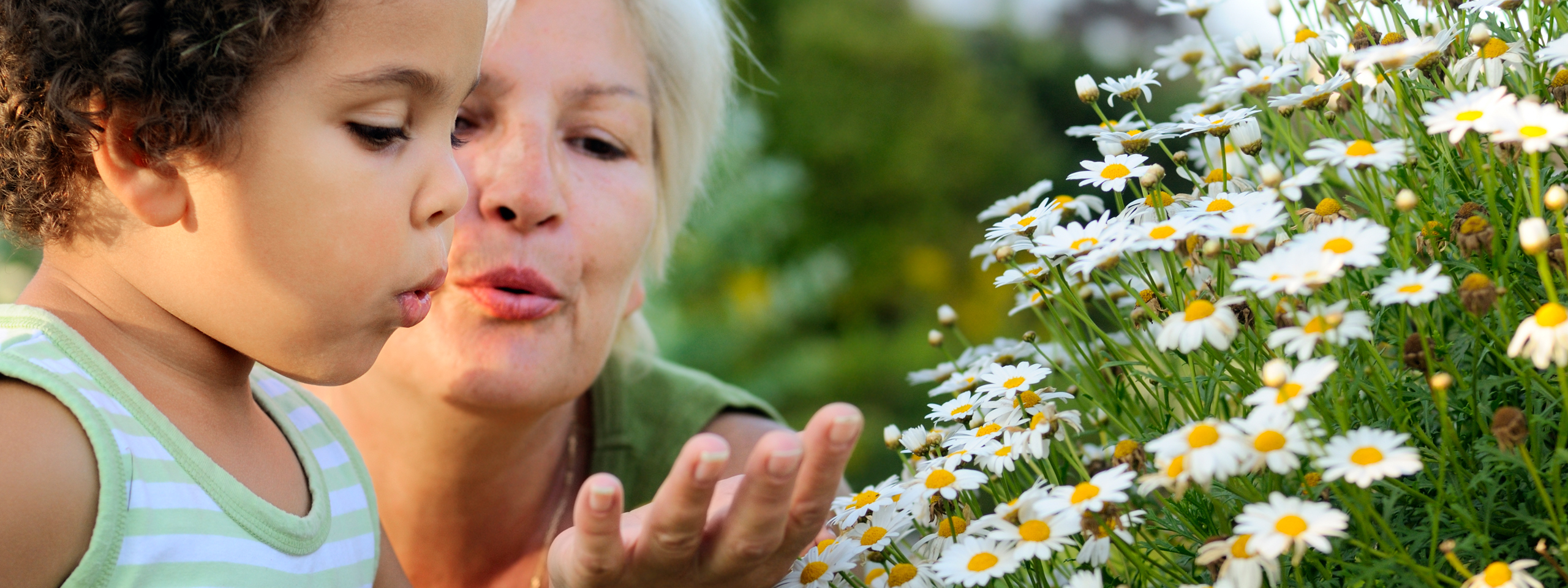 Frau, die Testamentsspende an SOS-Kinderdörfer getätigt hat, bläst mit Kind in Blumen hinein.