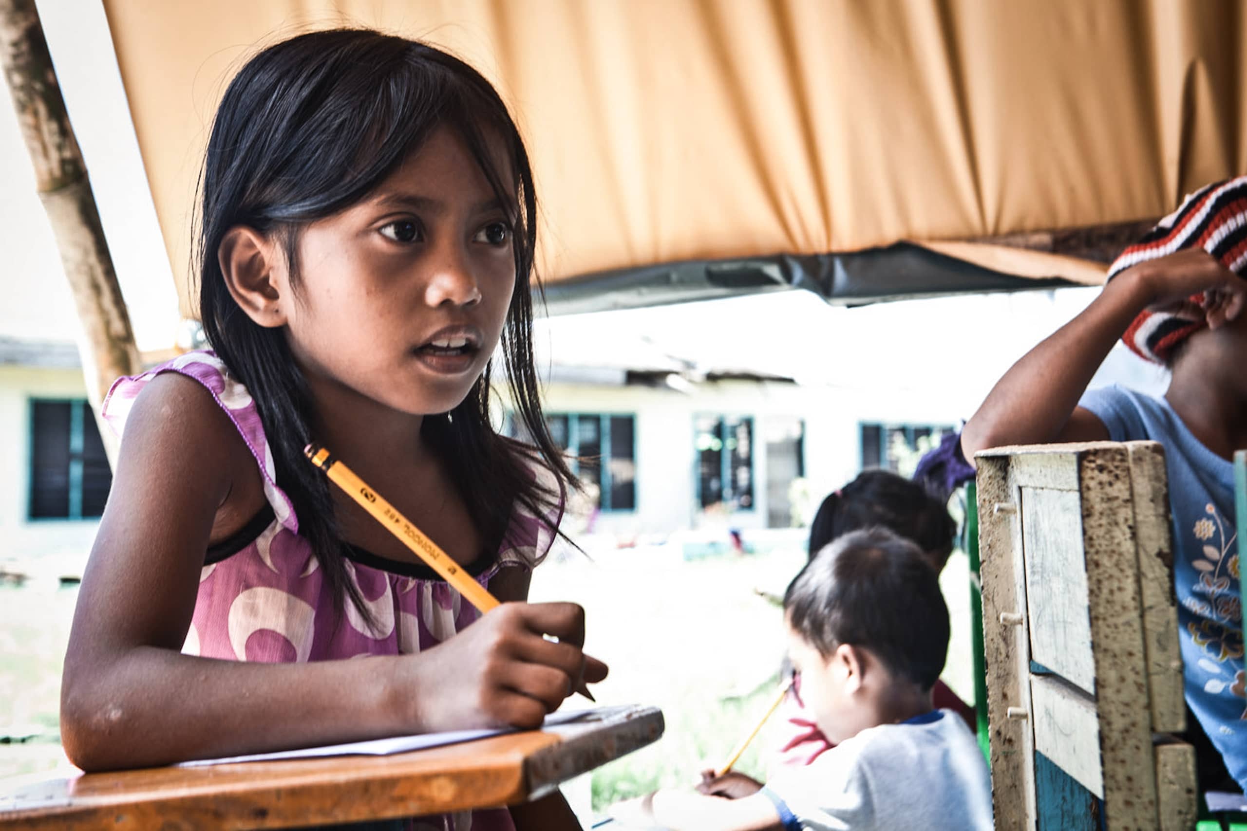 Mädchen schreibt mit einem Stift auf einem Blatt, profitiert von der Bildungsarbeit der SOS-Kinderdörfer weltweit.