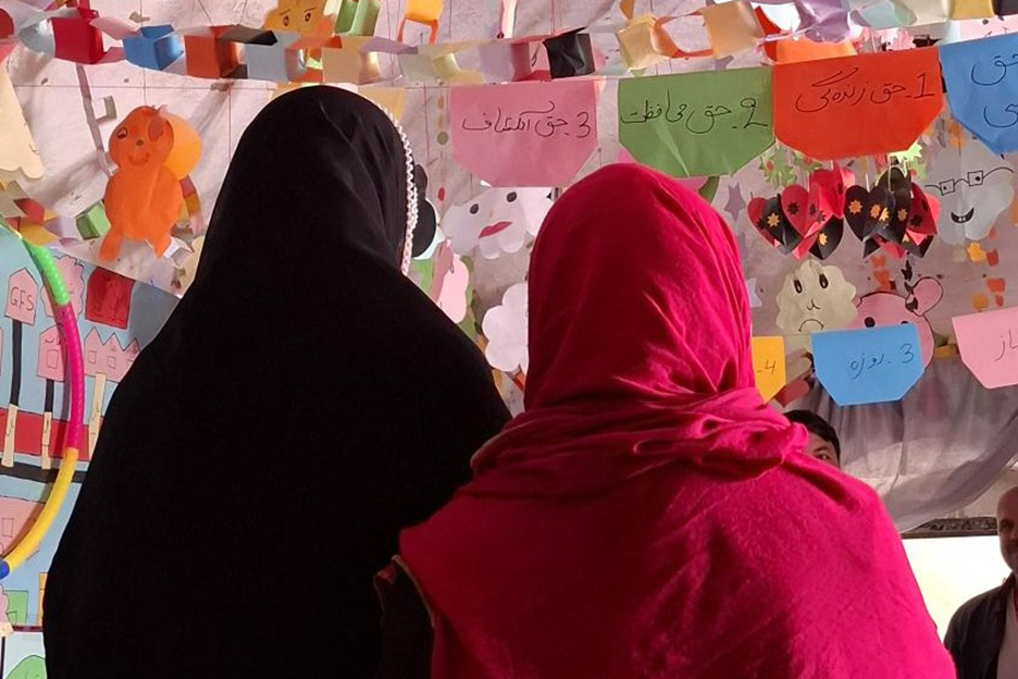 Ihre Rücken der Kamera zugewandt, schauen zwei Mädchen mit Hidschab, einem langen Kopftuch, auf eine mit Girlanden verzierte Decke. 