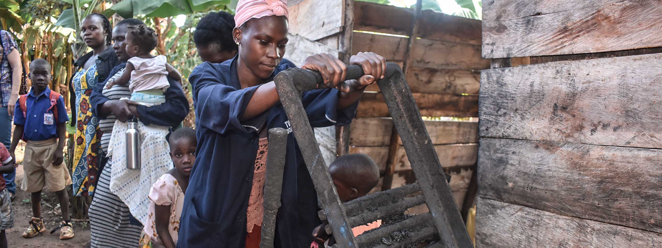 Frau in Uganda steht an einer Brikett-Presse.