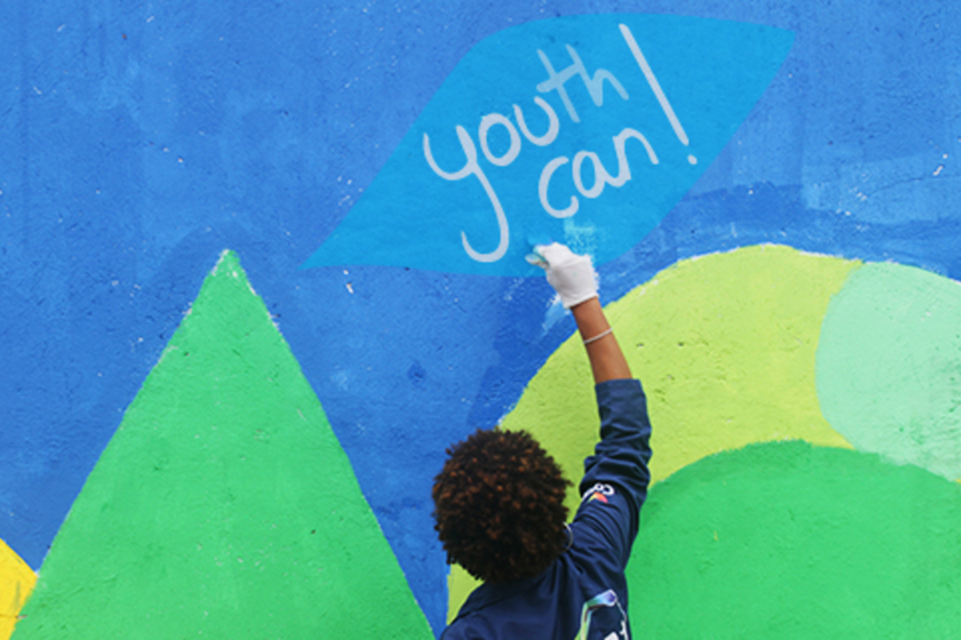 Ein Junge malt an eine bunte Wand den Slogan Youth Can