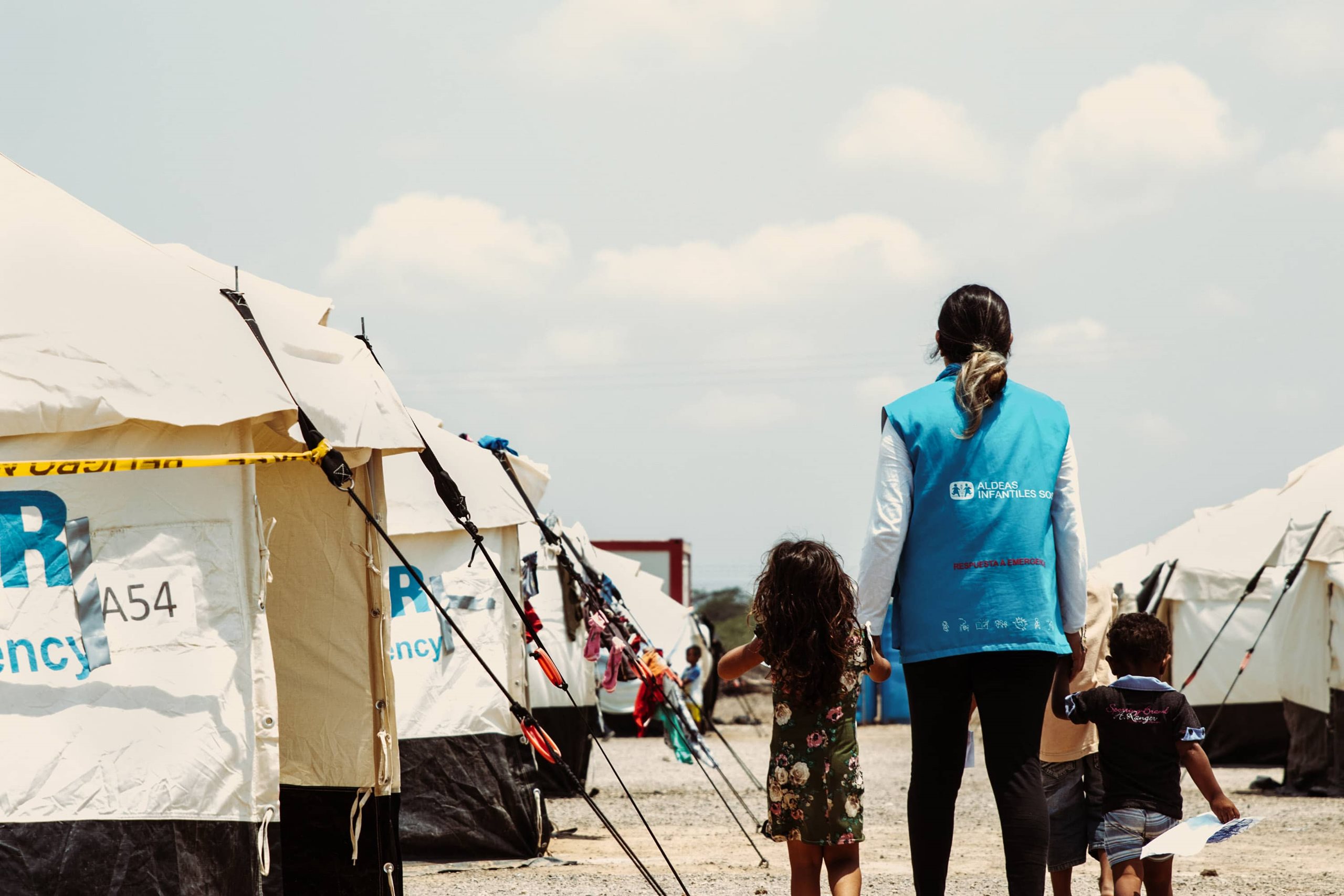 SOS-Kinderdorf-Mitarbeiterin geht mit einem Kind an der Hand in Nothilfe-Zentrum der SOS-Kinderdörfer weltweit.