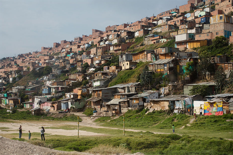 Eine Siedlung aus Wellblechhütten an einem Berghang in Bogotá/Kolumbien - im Vordergrund vier spielende Kinder.