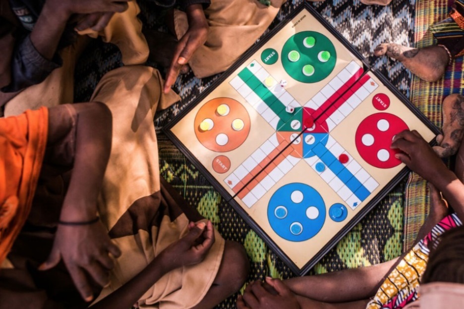 Kinder sitzen auf dem Boden um ein Spielbrett herum und spielen ,Ludo‘, die afrikanische Version von ,Mensch-ärgere-dich-nicht‘.