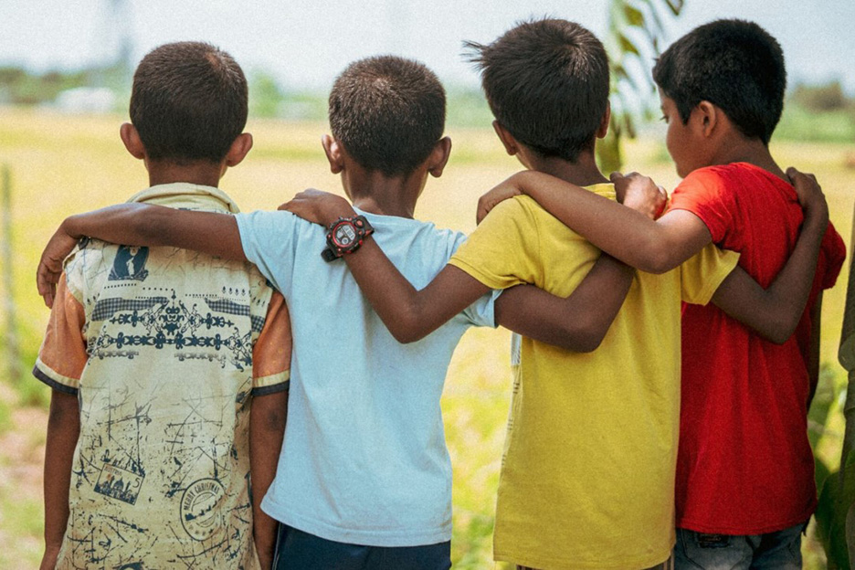 Vier Jungen stehen mit dem Rücken zur Kamera, währen einer dem andere den Arm über die Schultern legt.