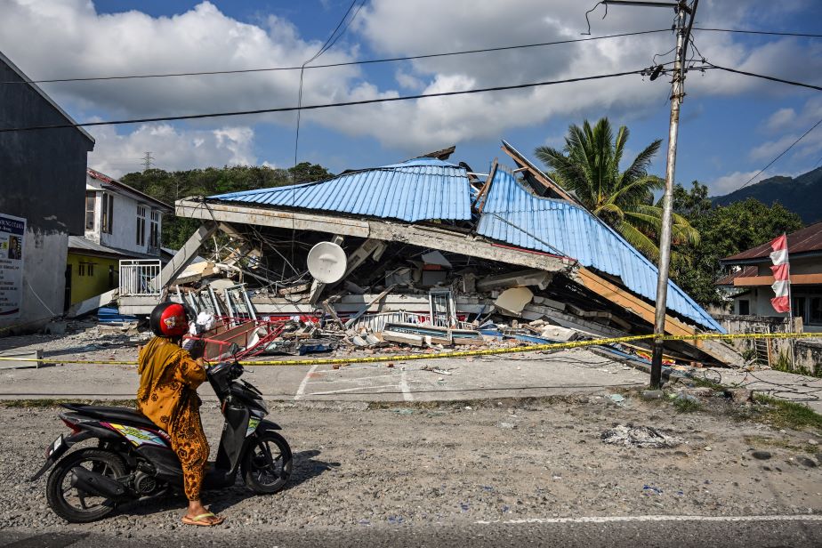 Ein eingestürztes Gebäude nach dem Erdbeben in Indonesien. Im Vordergrund steht eine Person mit einem Motorroller.
