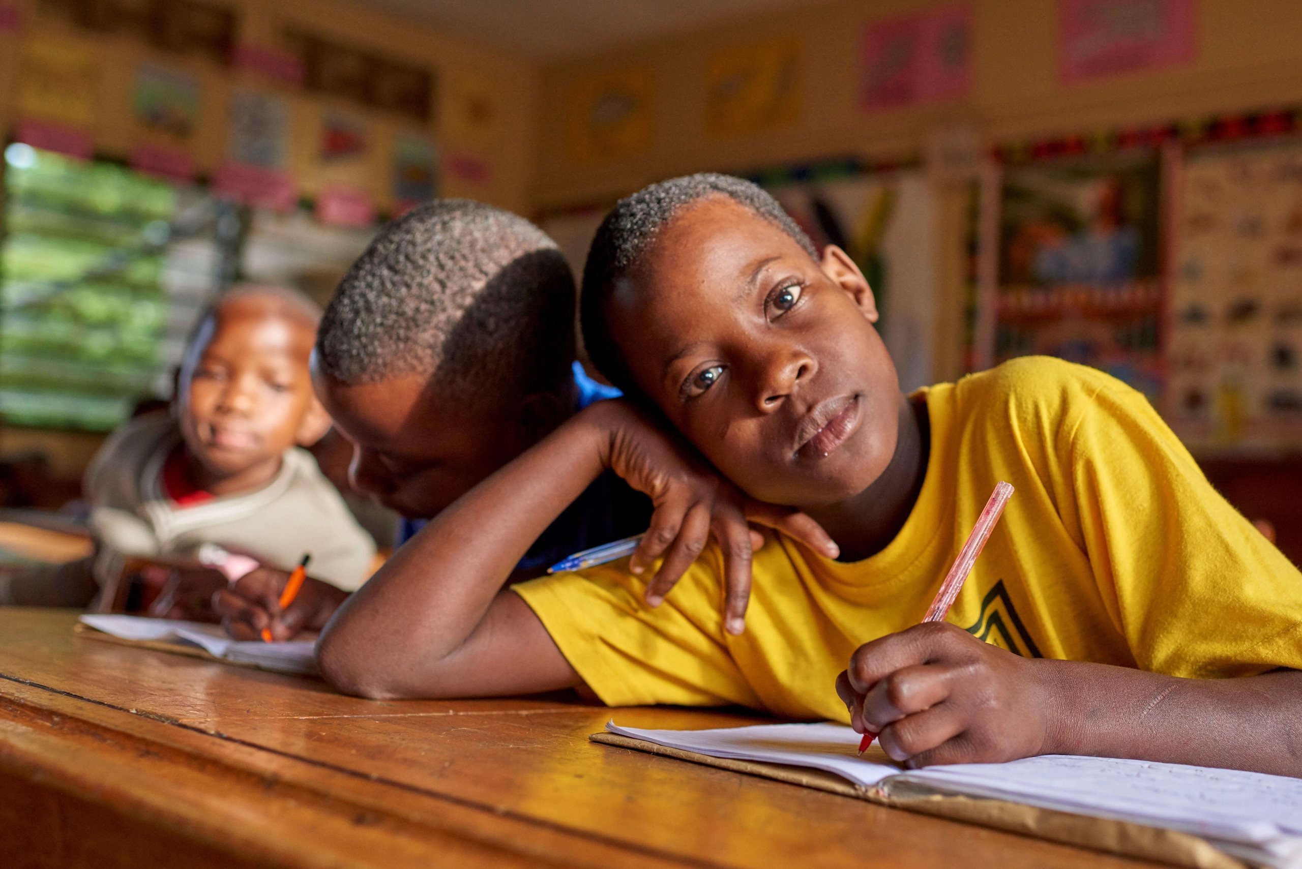 Junge sitzt an einer Schulbank und blickt in die Kamera, hofft auf eine Kinderpatenschaft.