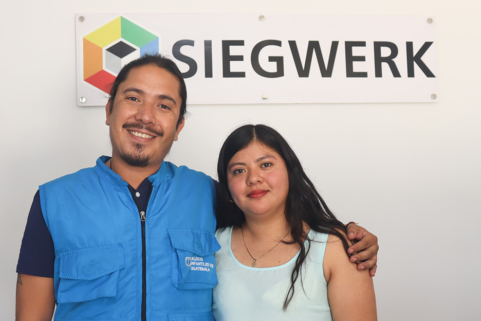 Ein Mitarbeiter der SOS-Kinderdörfer Guatemala mit einer Jugendlichen, vor dem Logo von Siegwerk.