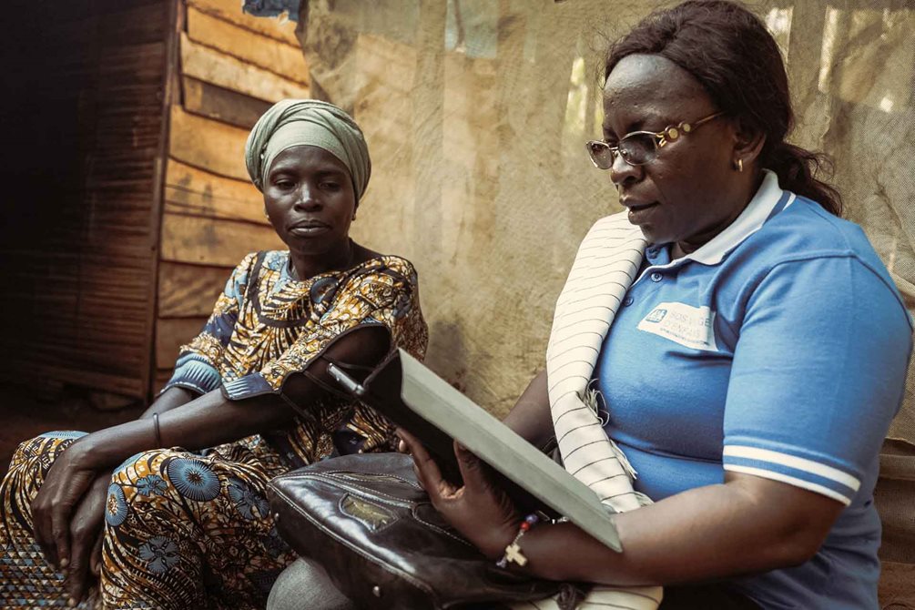 Eine Sozialarbeiterin der SOS-Kinderdörfer in DR Kongo bei einem ihrer Besuche bei einer Familie, die sie betreut. Die Ergebnisse des Entwicklungsgesprächs protokolliert die Sozialarbeiterin jetzt digital auf einem Tablet. Foto: Federico Varrasso