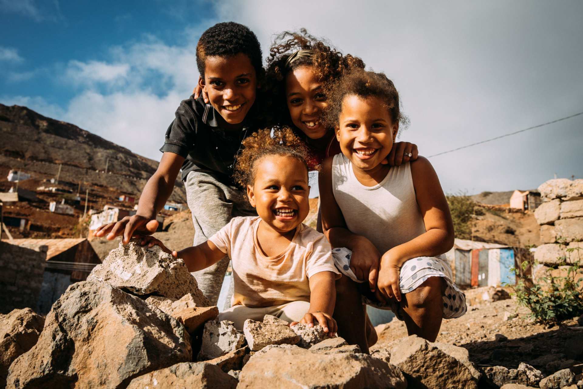 Vier Kinder sitzen im Freien auf Steinen und freuen sich über angekommene Spenden.