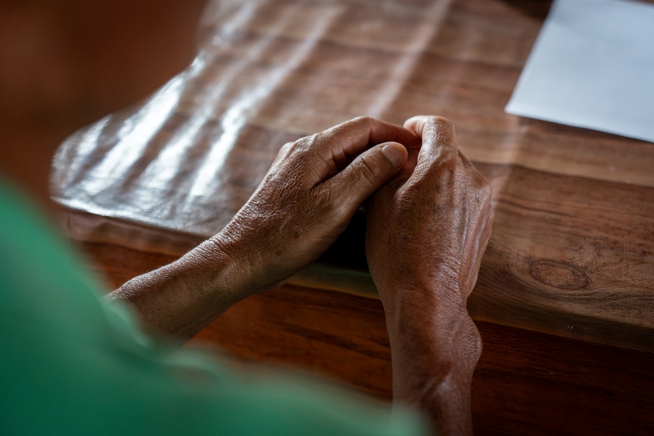 Gefaltete Hände liegen auf einem Holztisch.