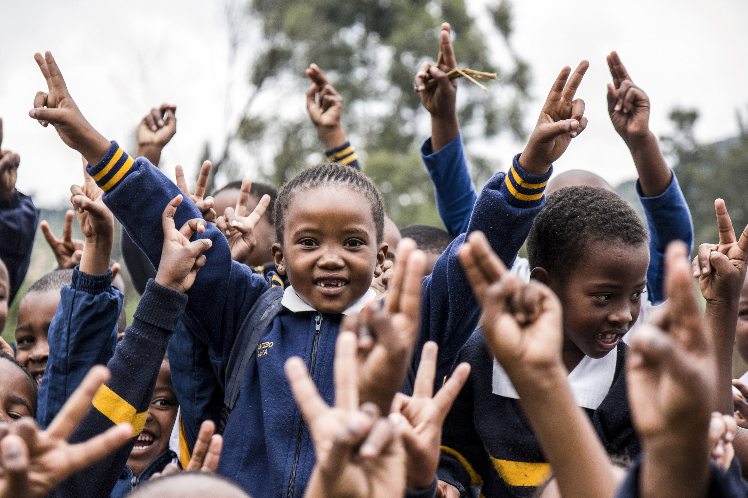Viele Kinder halten Hände in die Luft, formen Victory-Zeichen, repräsentieren Einsatz für Kinderrechte.
