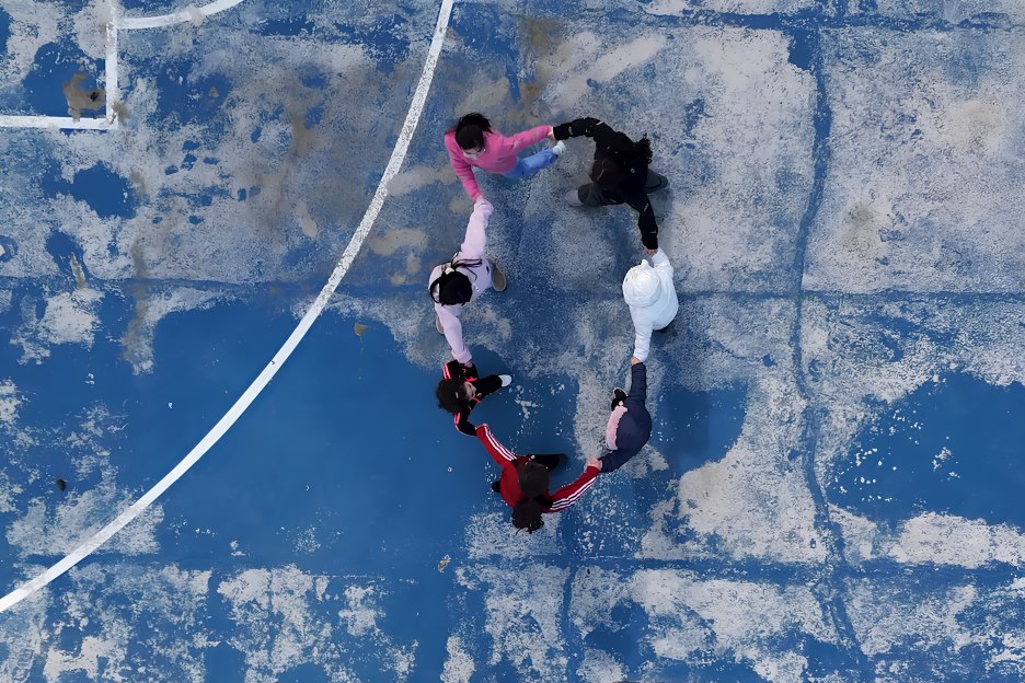 Mehrere Kinder halten sich an den Händen und bilden auf einem blauen Spielfeld einen Kreis.