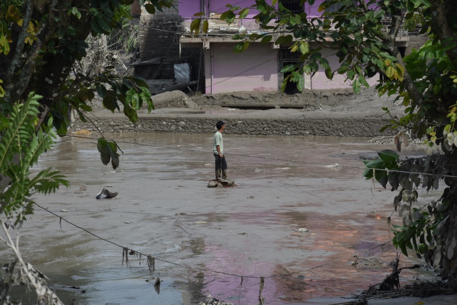 Ein Mann steht in einer von Schlamm und Wasser überfluteten Straße vor beschädigten Häusern in Nepal.