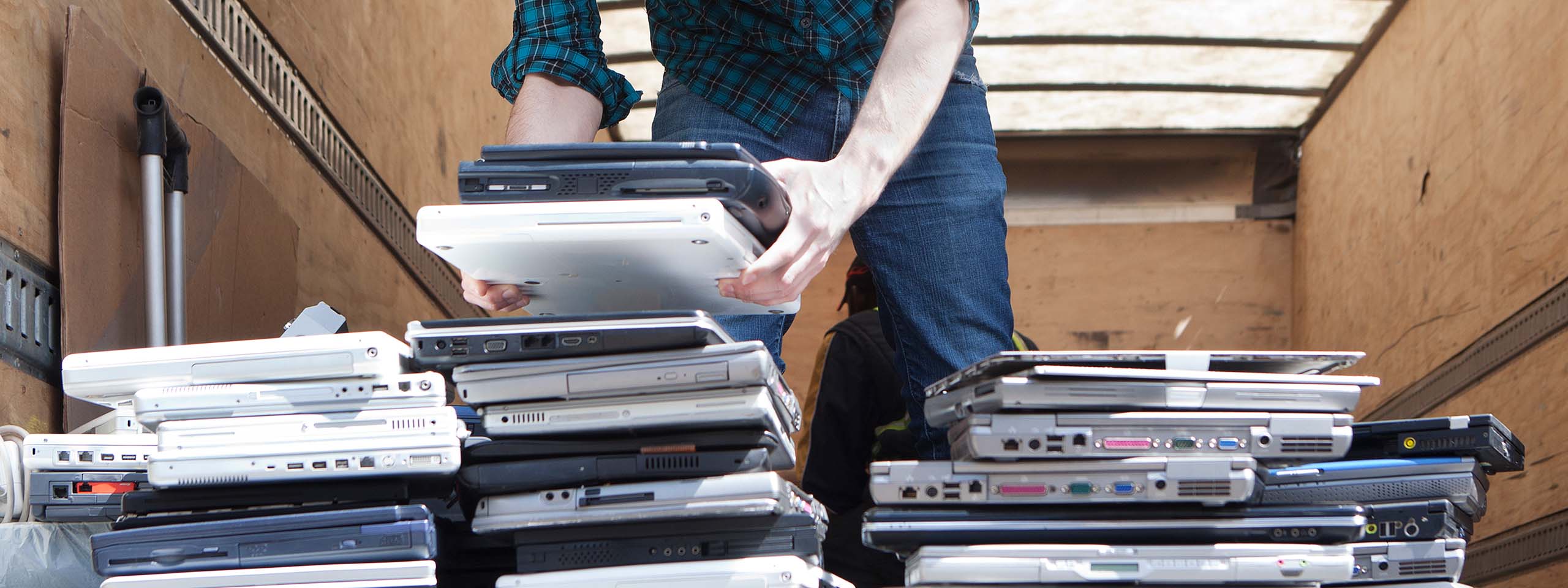 Eine Person nimmt mit beiden Händen einen Stapel Laptops auf.