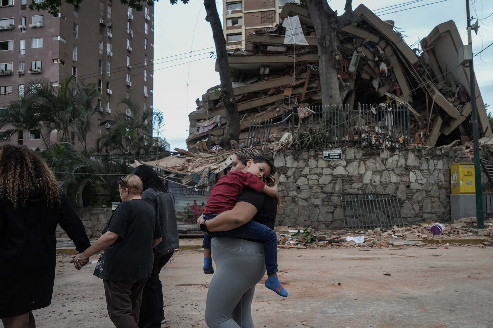 Kind auf dem Arm einer Frau, Trümmer im Hintergrund, Foto: AFP