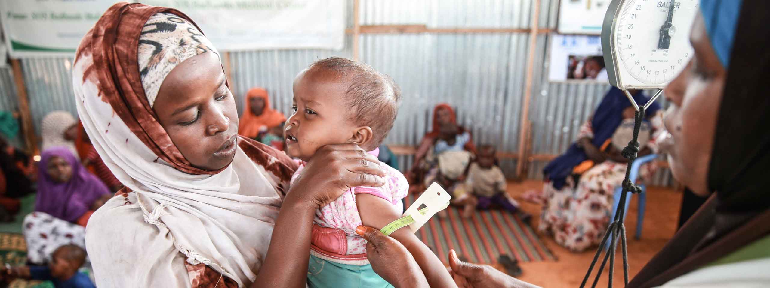 Ein Baby wird von einer Mitarbeiterin der SOS-Kinderdörfer auf Mangelernährung untersucht. 