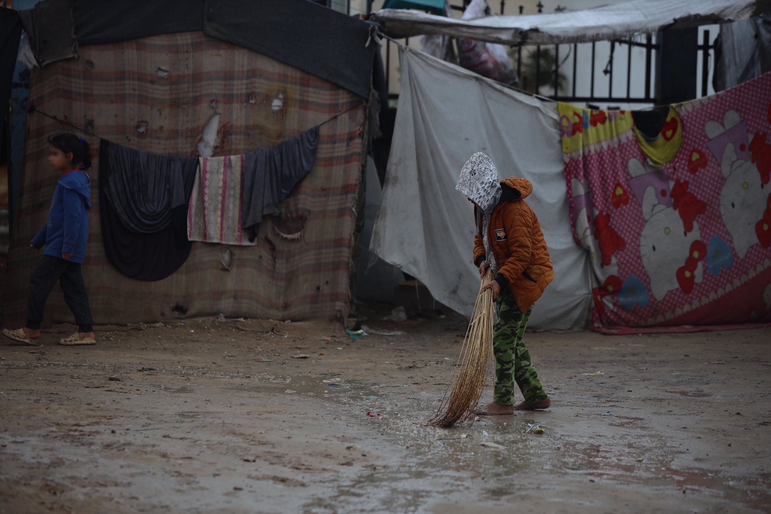 Ein Junge in einem Flüchtlingscamp fegt Wasser von einem überschwemmten Weg