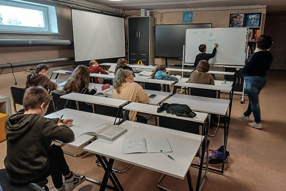 Kinder sitzen im Keller an Schultischen.