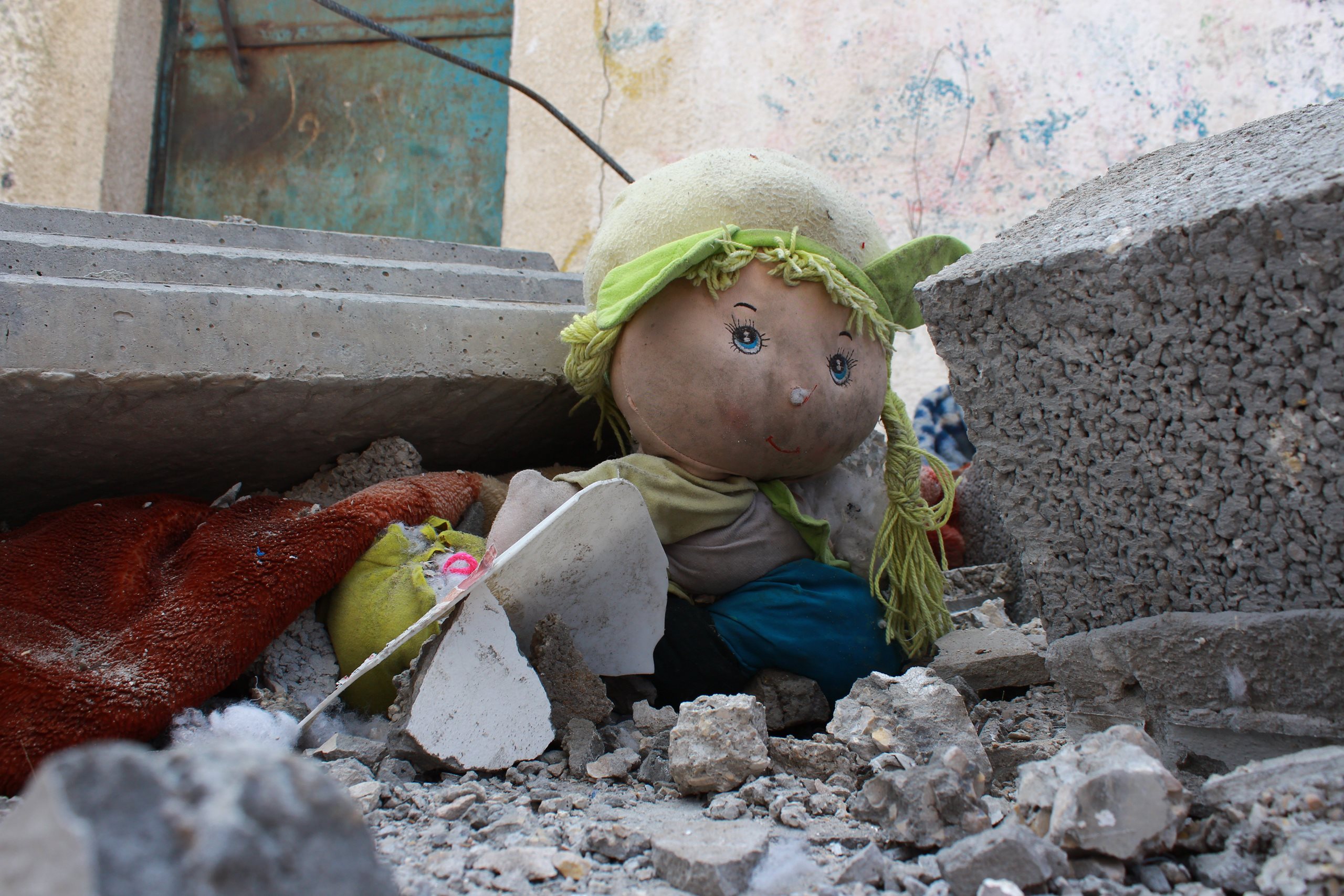Zwischen den Trümmern eines Hauses sitzt eine Stoffpuppe.