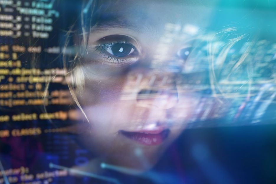 Ein junges Mädchen, das sich in der digitalen Welt bewegt. Dies wird durch die Spiegelung eines Bildschirms und Formeln deutlich. 